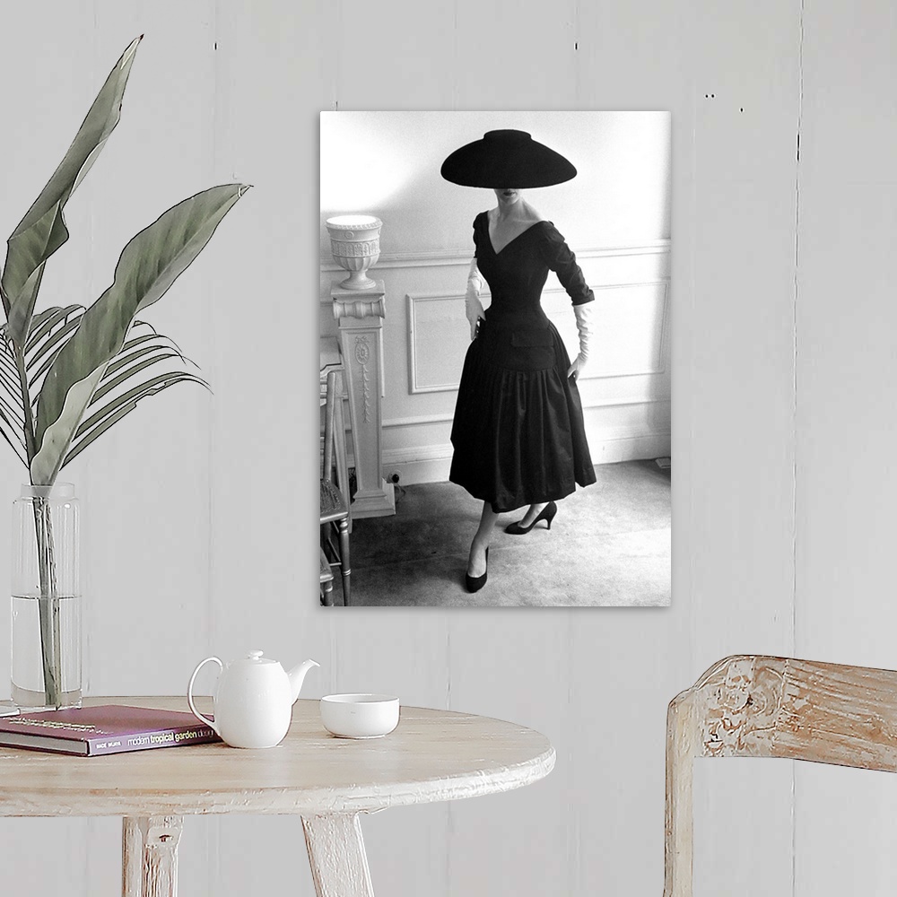 A farmhouse room featuring A model wearing a black cocktail dress and a black velvet wide-brimmed hat, designed by Ronald Pa...