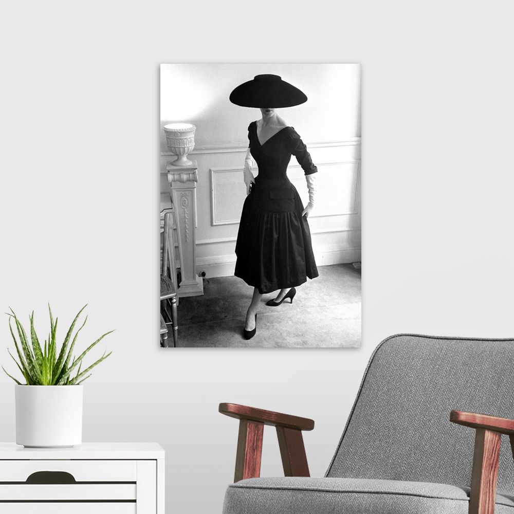 A modern room featuring A model wearing a black cocktail dress and a black velvet wide-brimmed hat, designed by Ronald Pa...