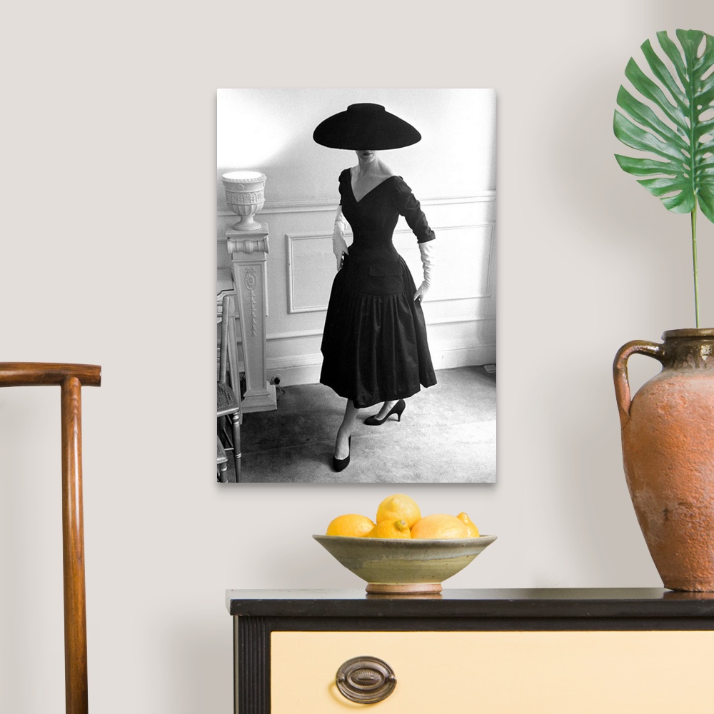 A traditional room featuring A model wearing a black cocktail dress and a black velvet wide-brimmed hat, designed by Ronald Pa...