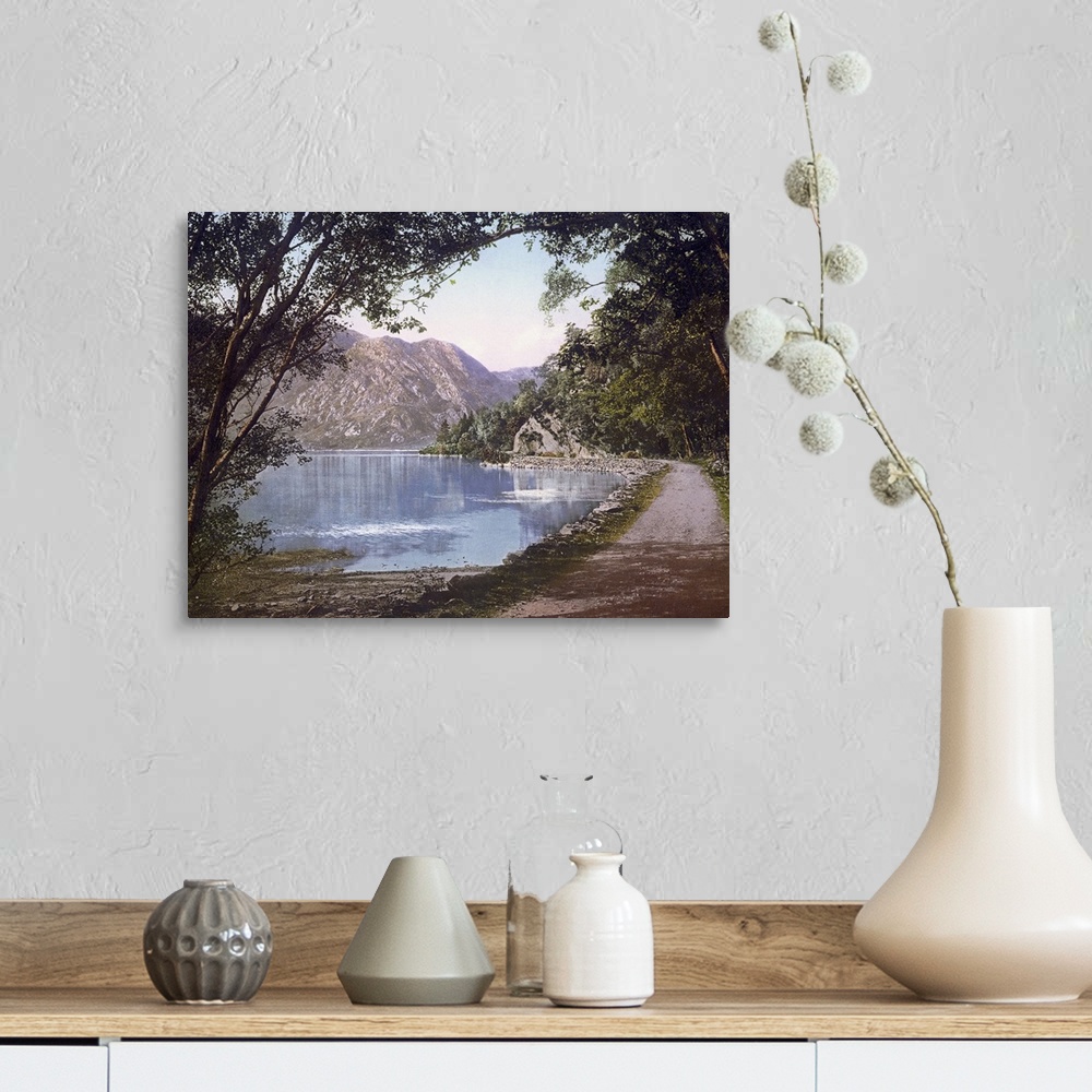A farmhouse room featuring A vintage shot of a gravel path winding its way at the water's edge as leafy trees and cliffs loo...
