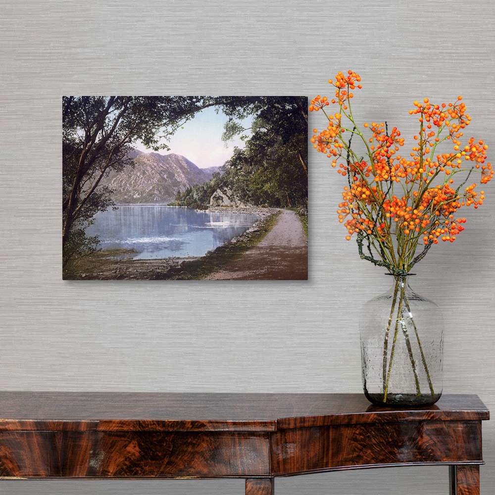 A traditional room featuring A vintage shot of a gravel path winding its way at the water's edge as leafy trees and cliffs loo...