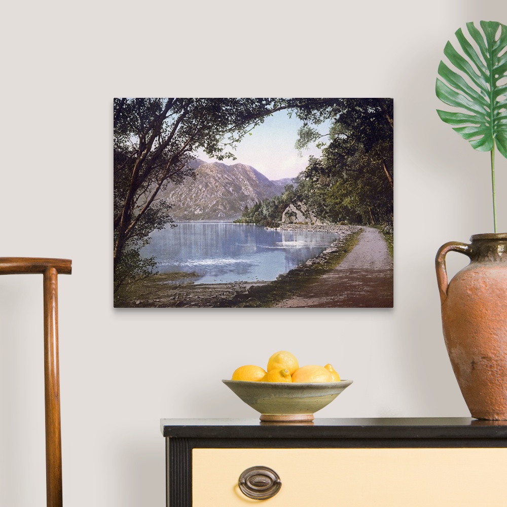A traditional room featuring A vintage shot of a gravel path winding its way at the water's edge as leafy trees and cliffs loo...