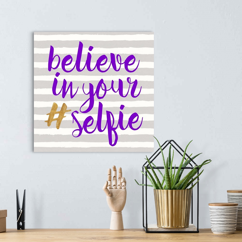 A bohemian room featuring "Believe in Your (hashtag) Selfie" written in purple and gold on a gray and white striped backgro...