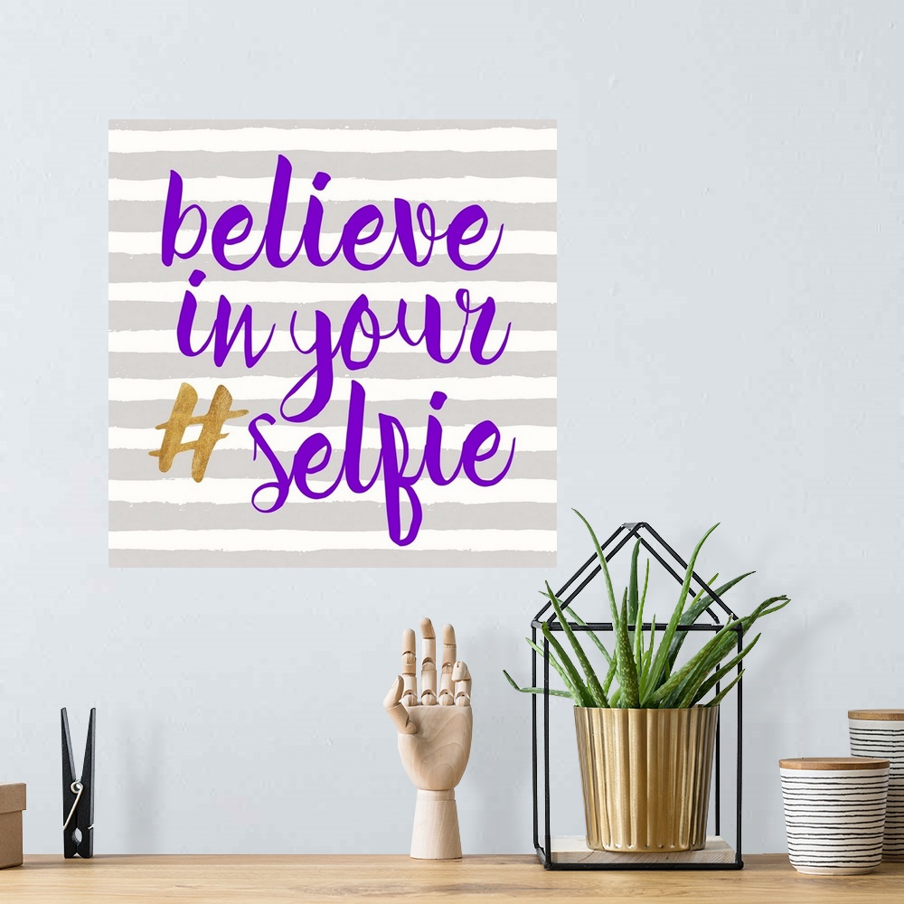A bohemian room featuring "Believe in Your (hashtag) Selfie" written in purple and gold on a gray and white striped backgro...
