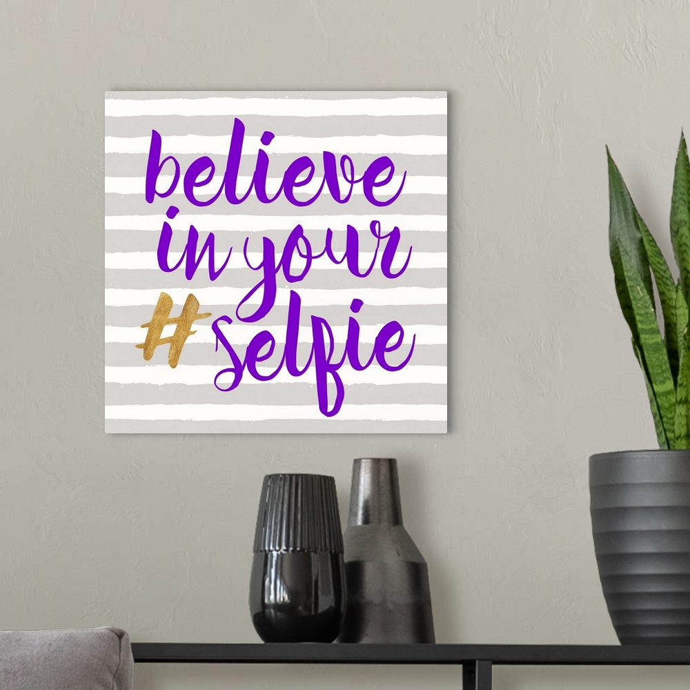 A modern room featuring "Believe in Your (hashtag) Selfie" written in purple and gold on a gray and white striped backgro...