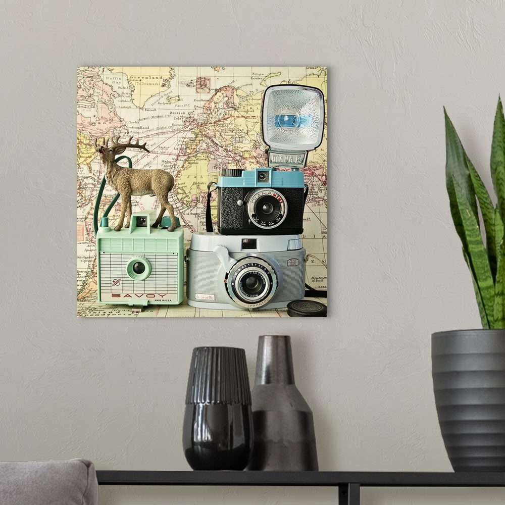 A modern room featuring A toy deer on a set of three vintage cameras with a map backdrop.