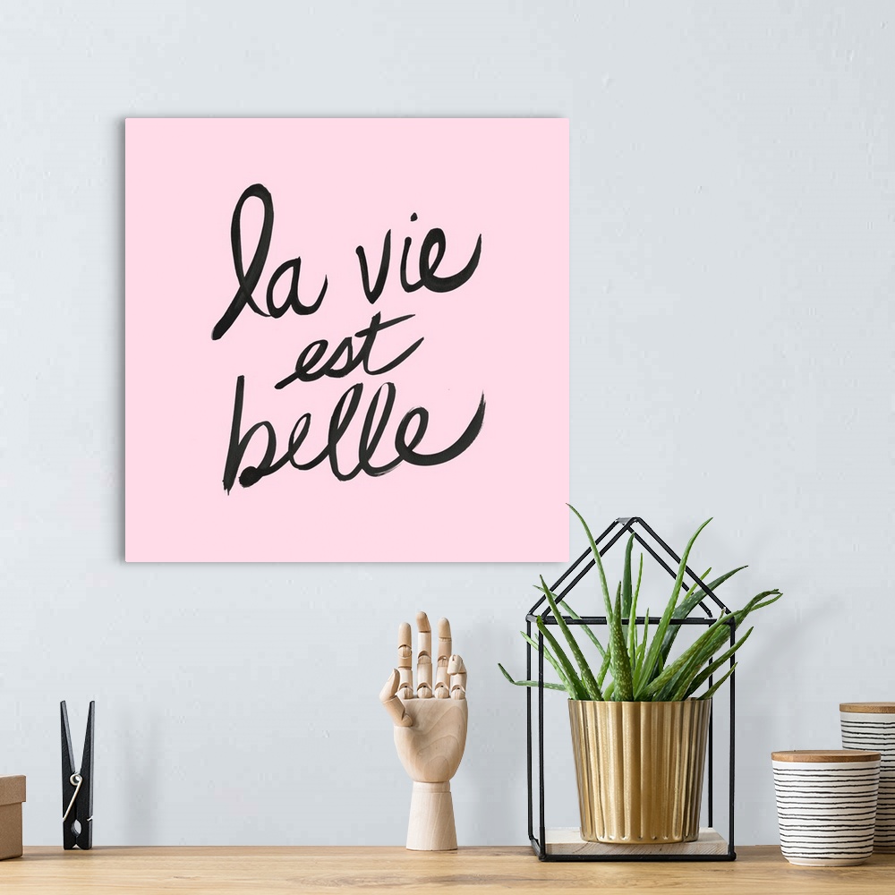 A bohemian room featuring "La Vie Est Belle" hand lettered in black on a pastel pink background.