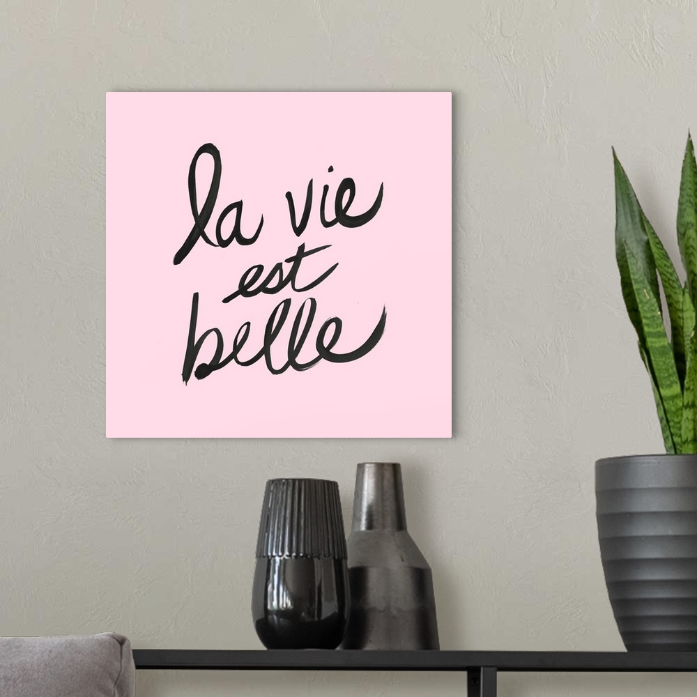 A modern room featuring "La Vie Est Belle" hand lettered in black on a pastel pink background.