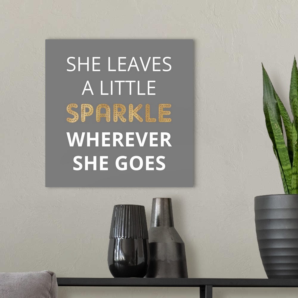 A modern room featuring Typography art reading "She leaves a little sparkle wherever she goes" in white and gold on grey.