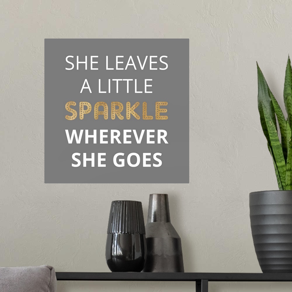 A modern room featuring Typography art reading "She leaves a little sparkle wherever she goes" in white and gold on grey.