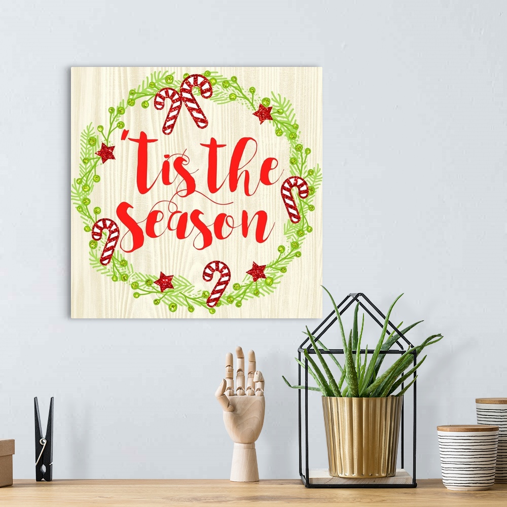 A bohemian room featuring "Tis The Season" written in red inside of a Christmas wreath on a faux wood background.