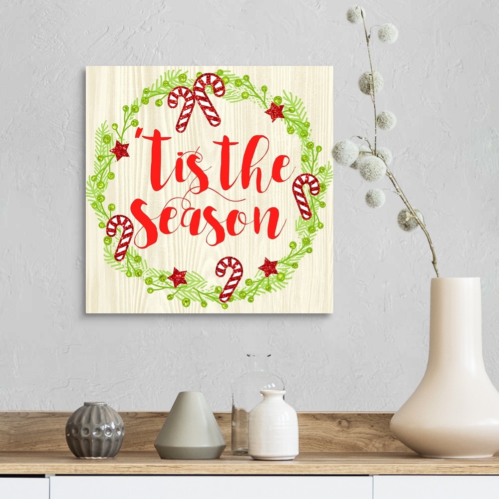 A farmhouse room featuring "Tis The Season" written in red inside of a Christmas wreath on a faux wood background.