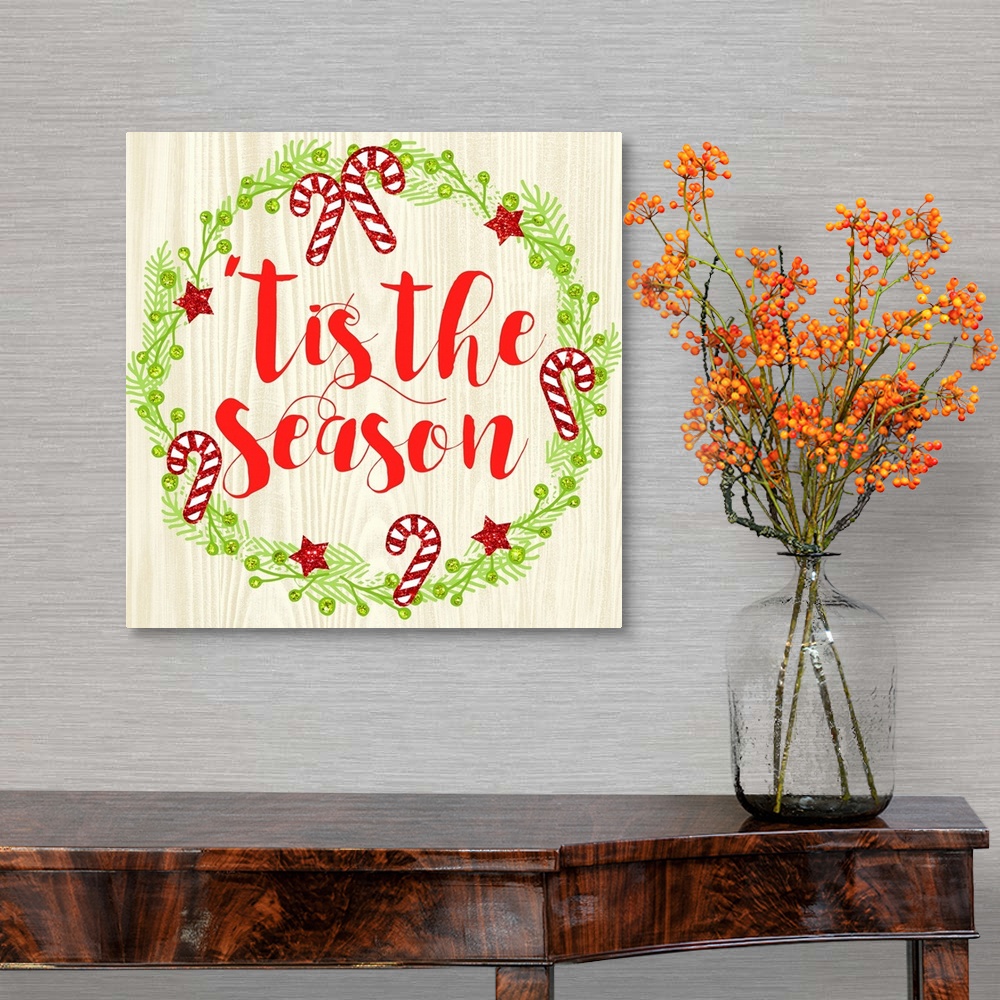 A traditional room featuring "Tis The Season" written in red inside of a Christmas wreath on a faux wood background.