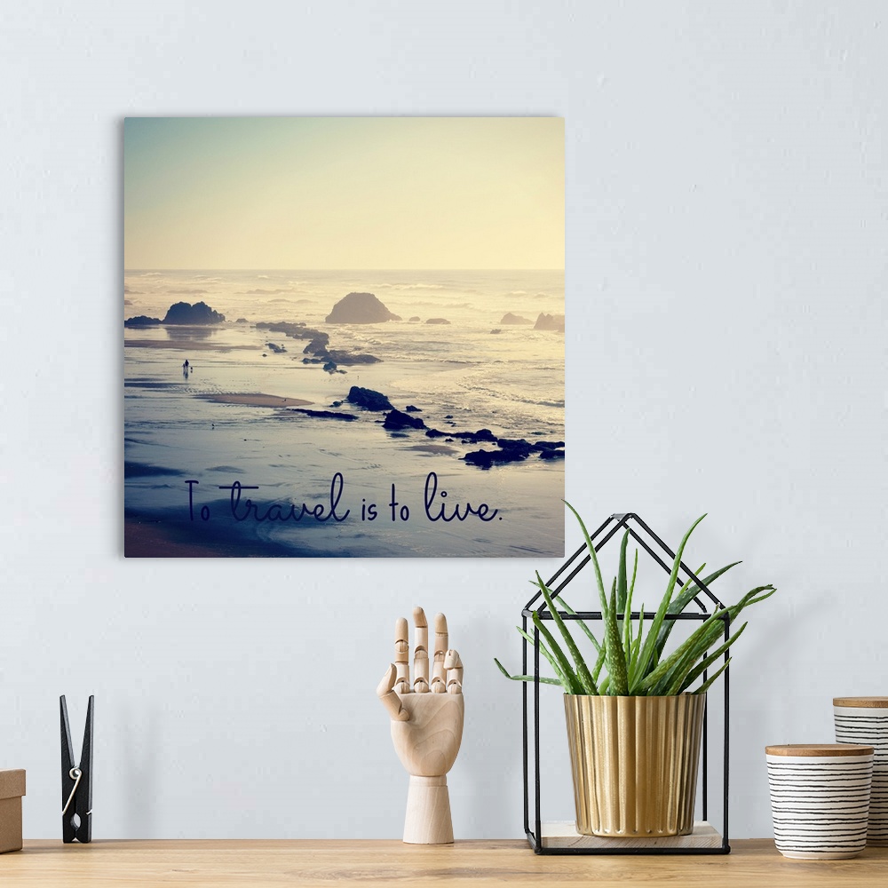 A bohemian room featuring "To Travel Is To Live" written at the bottom of a square photograph of a rocky beach shore.
