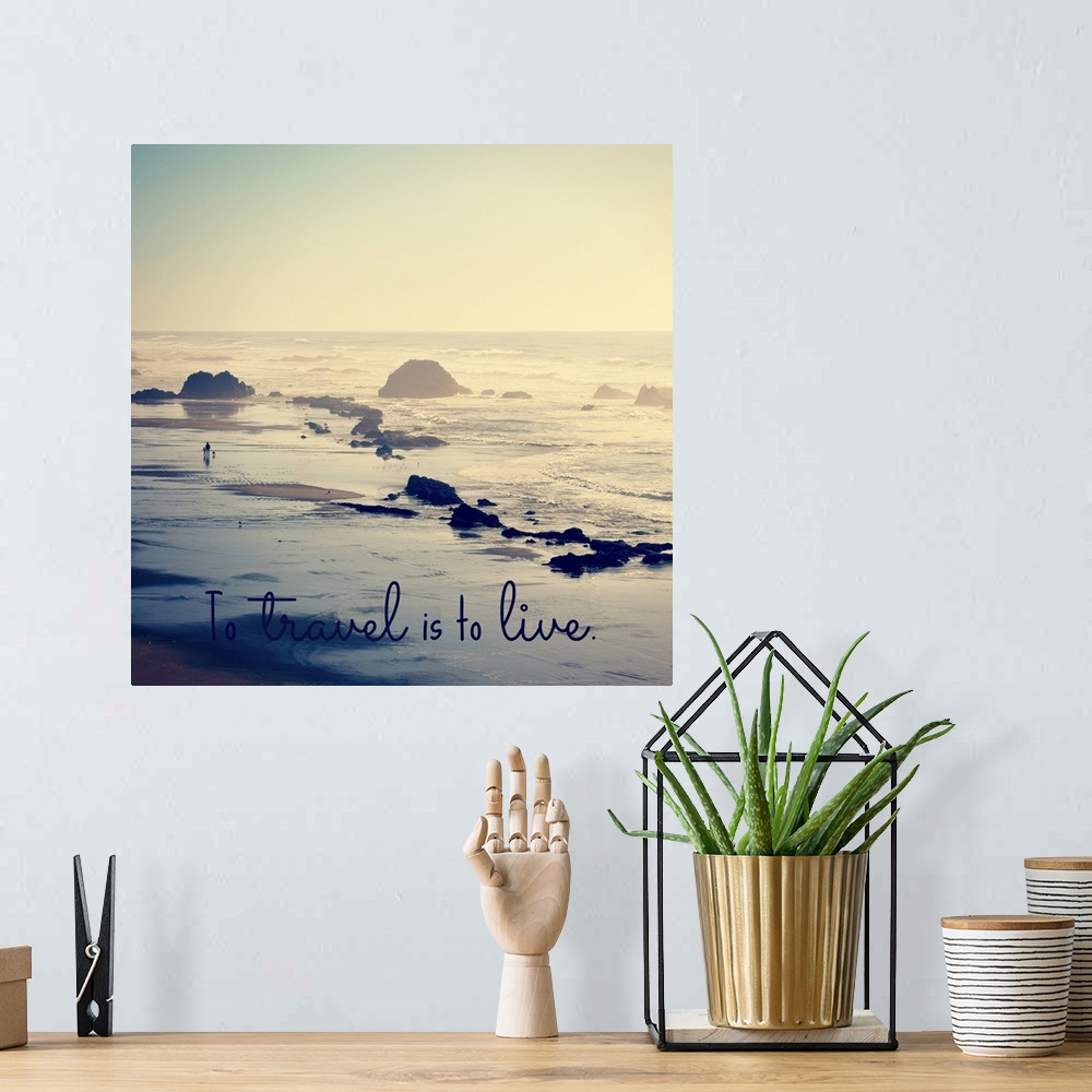 A bohemian room featuring "To Travel Is To Live" written at the bottom of a square photograph of a rocky beach shore.