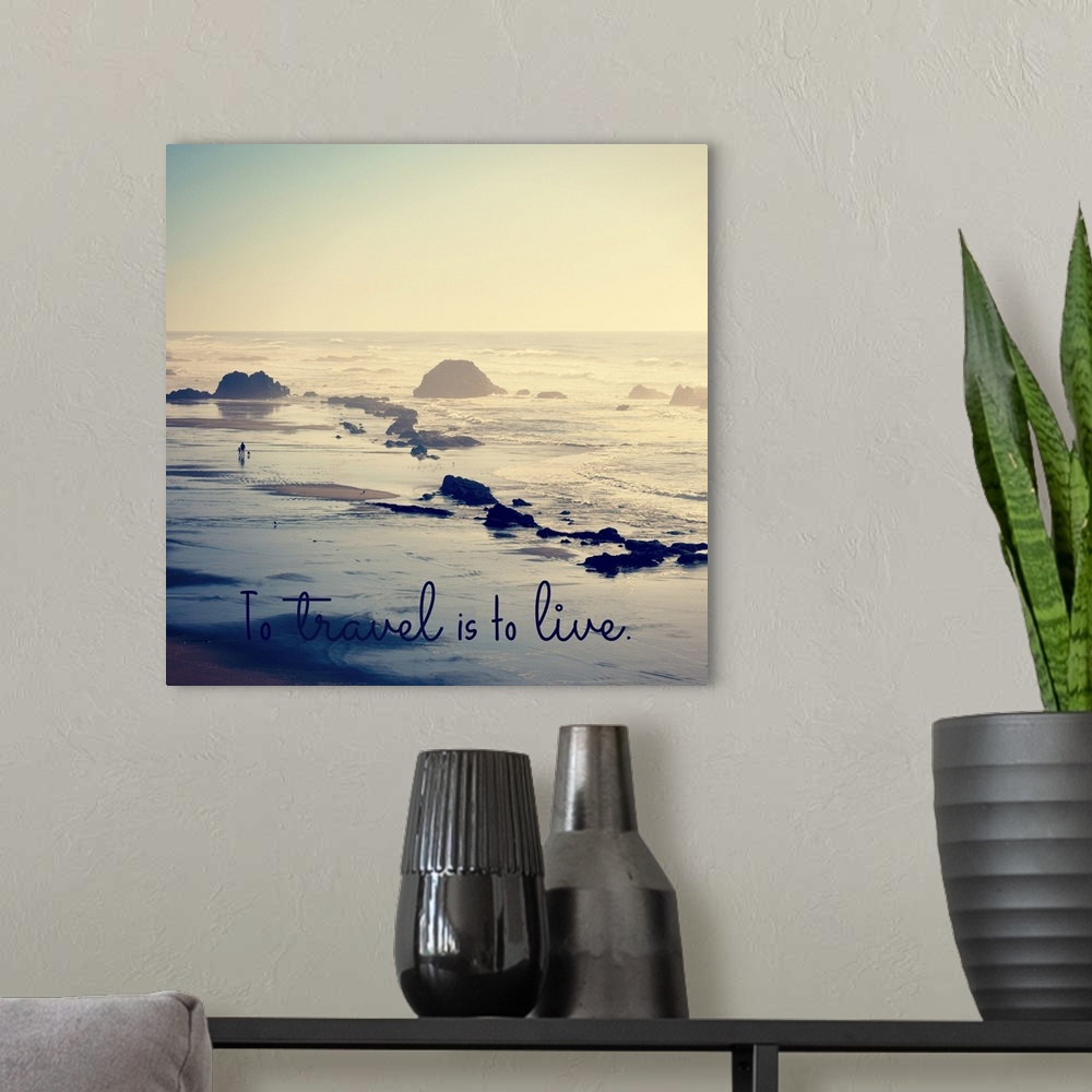 A modern room featuring "To Travel Is To Live" written at the bottom of a square photograph of a rocky beach shore.
