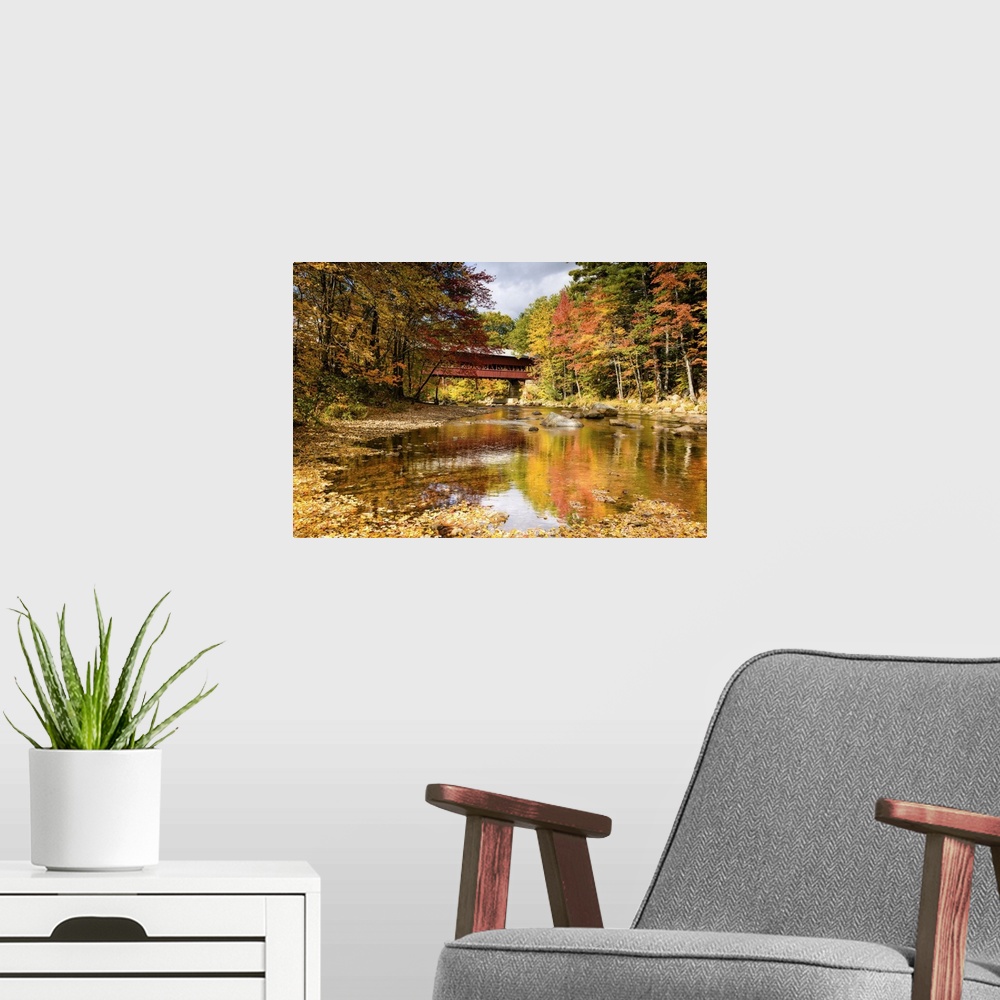 A modern room featuring A photograph of a covered bridge spanning a stream in a forest in autumn foliage.