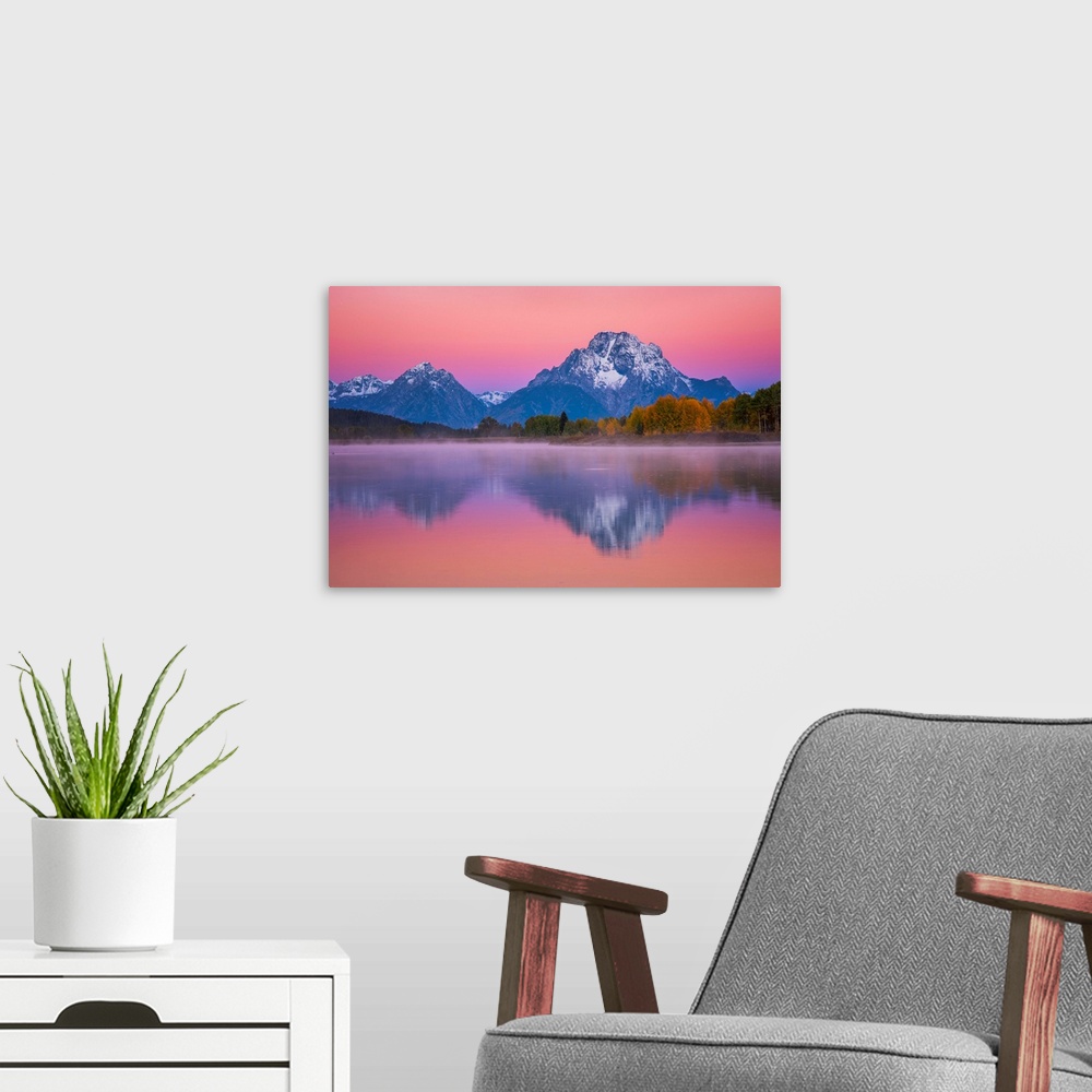 A modern room featuring Snow-capped mountains under a pink sunset sky reflected in a lake.