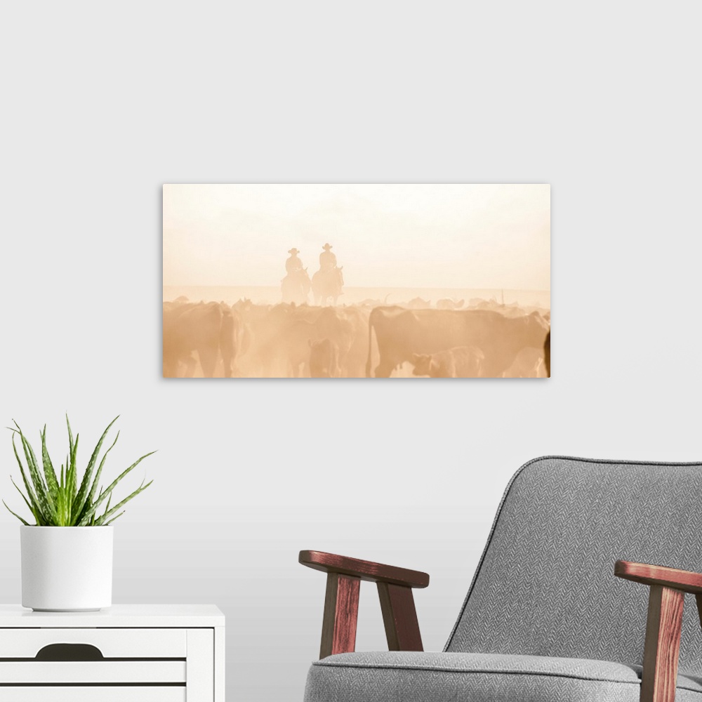 A modern room featuring Blown out photograph with sepia silhouettes of two people on horseback behind a dusty herd of cat...