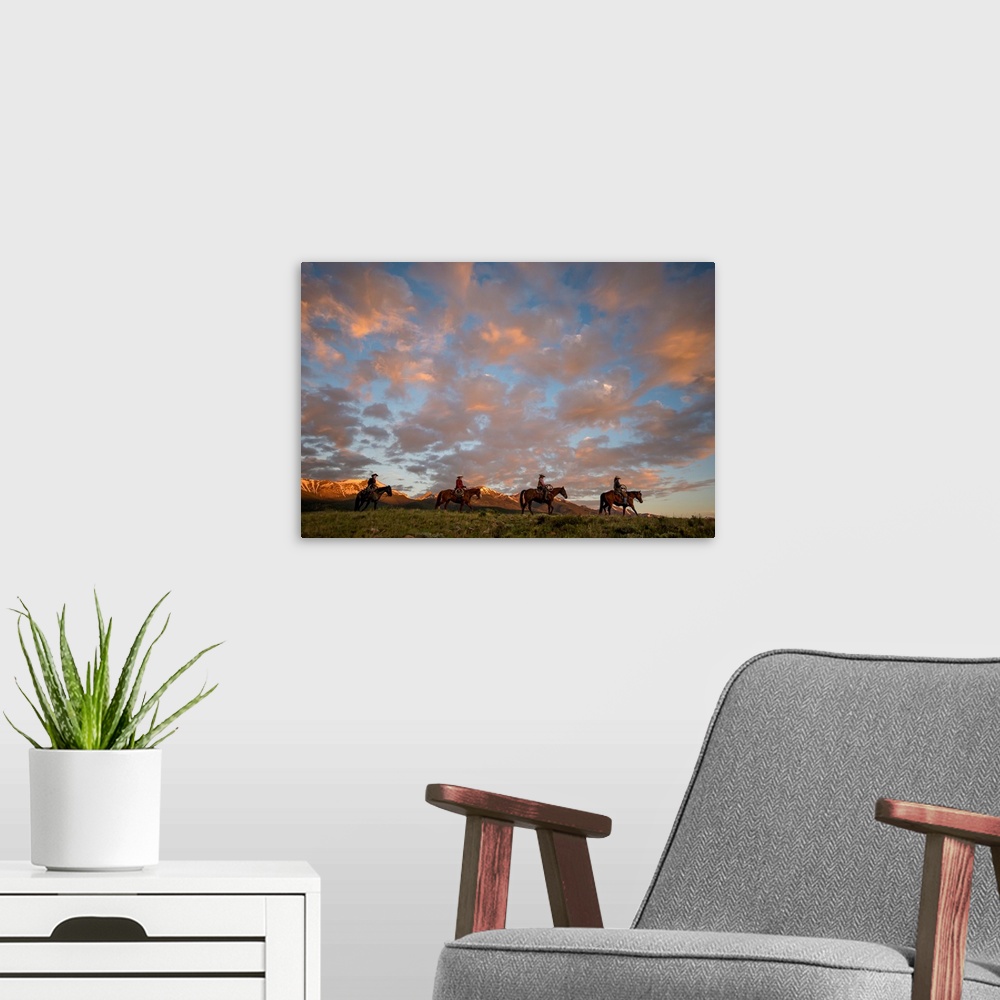 A modern room featuring Sunset photograph with four people on horseback riding through a valley in a line with snow cappe...