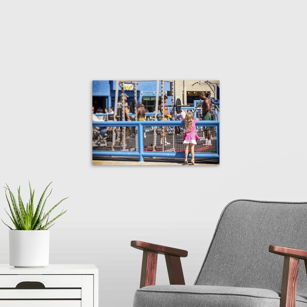 A modern room featuring Curiosity, Muscle Beach, young girl watching muscle men, color photograph