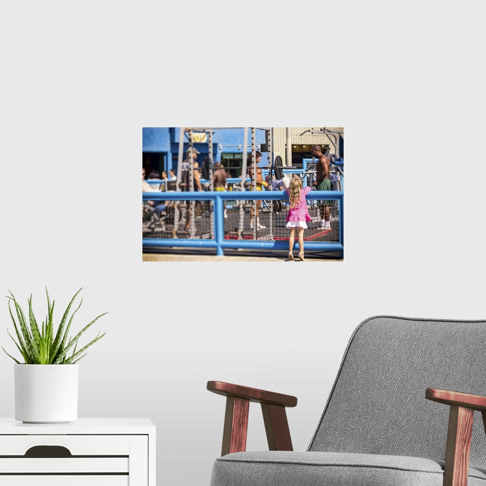 A modern room featuring Curiosity, Muscle Beach, young girl watching muscle men, color photograph