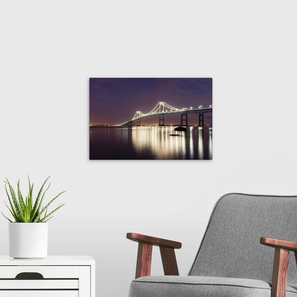 A modern room featuring A photograph of a large suspension bridge seen lit up at night casting long reflections on the wa...