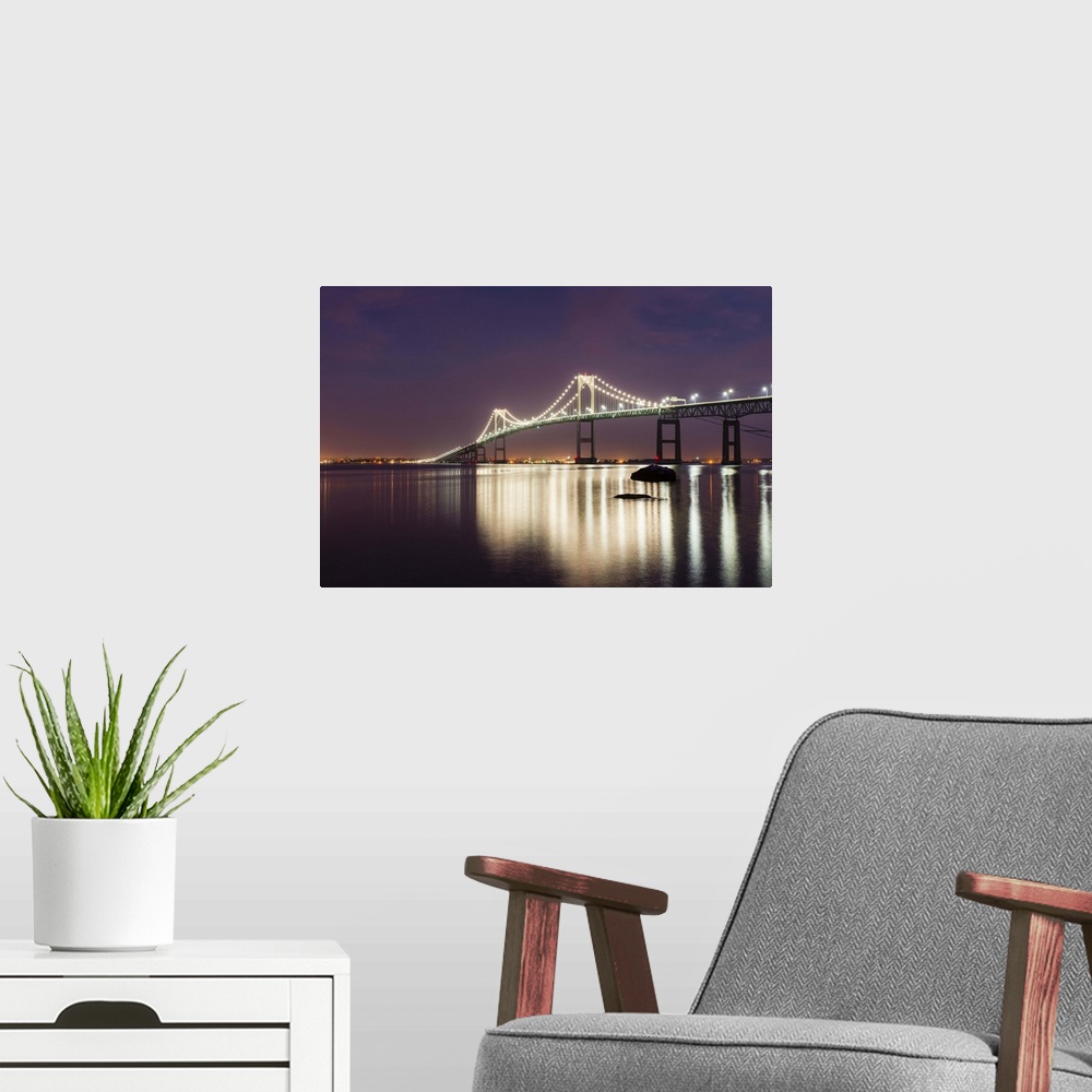 A modern room featuring A photograph of a large suspension bridge seen lit up at night casting long reflections on the wa...