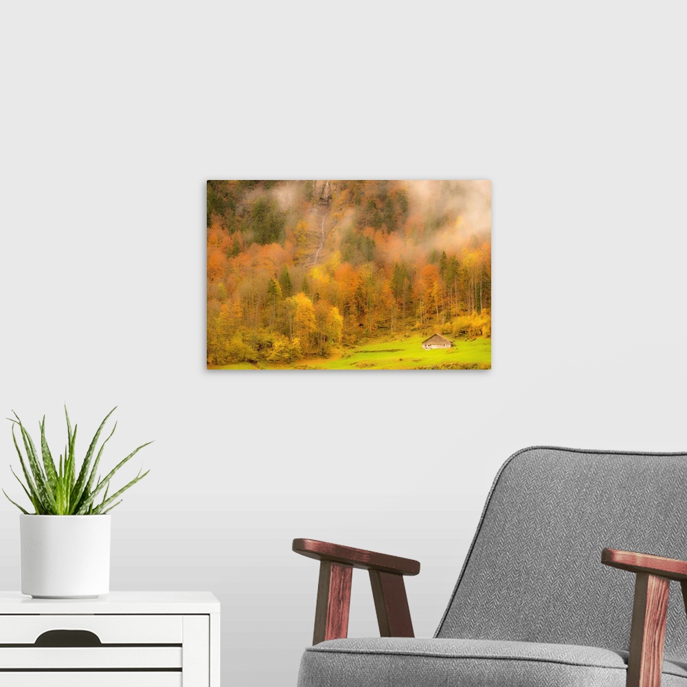 A modern room featuring Landscape photograph of colorful Autumn trees on the side of a foggy mountain with a small cabin ...