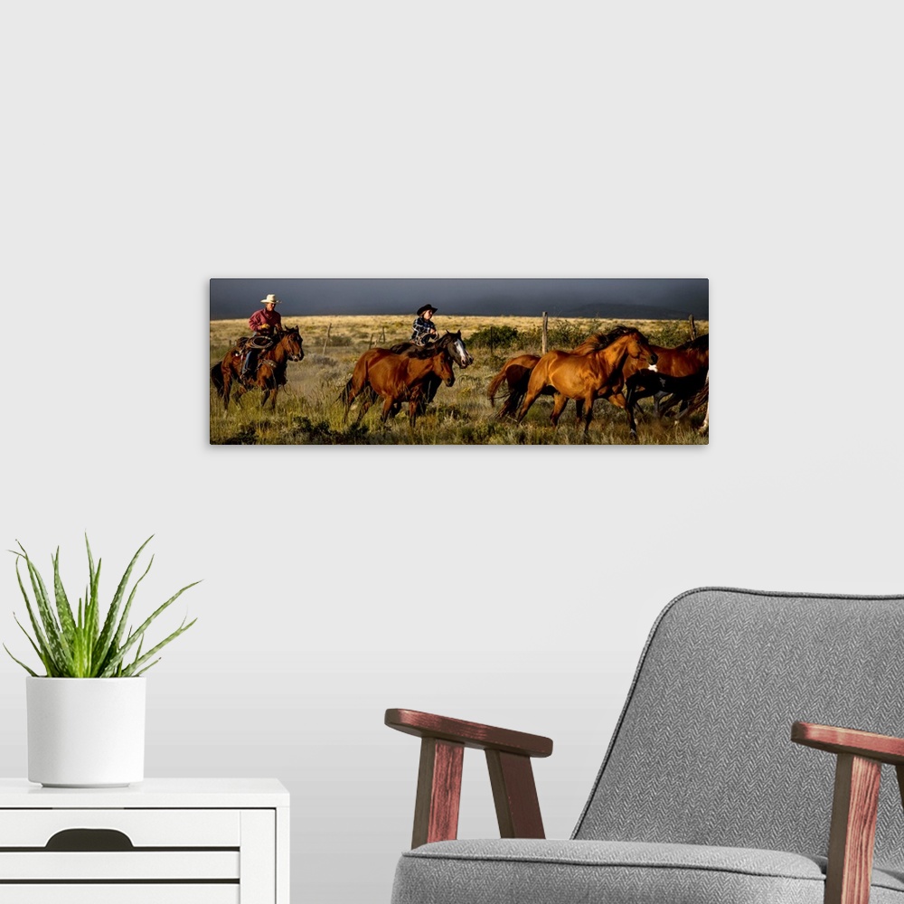 A modern room featuring Action photograph of two cowgirls herding horses with a dark sky in the distance.