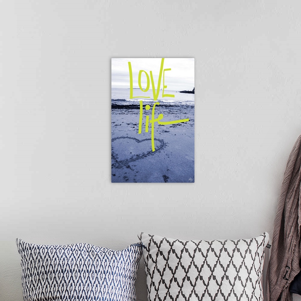 A bohemian room featuring "Love Life" handwritten over a photograph of a heart drawn in the sand on a beach.