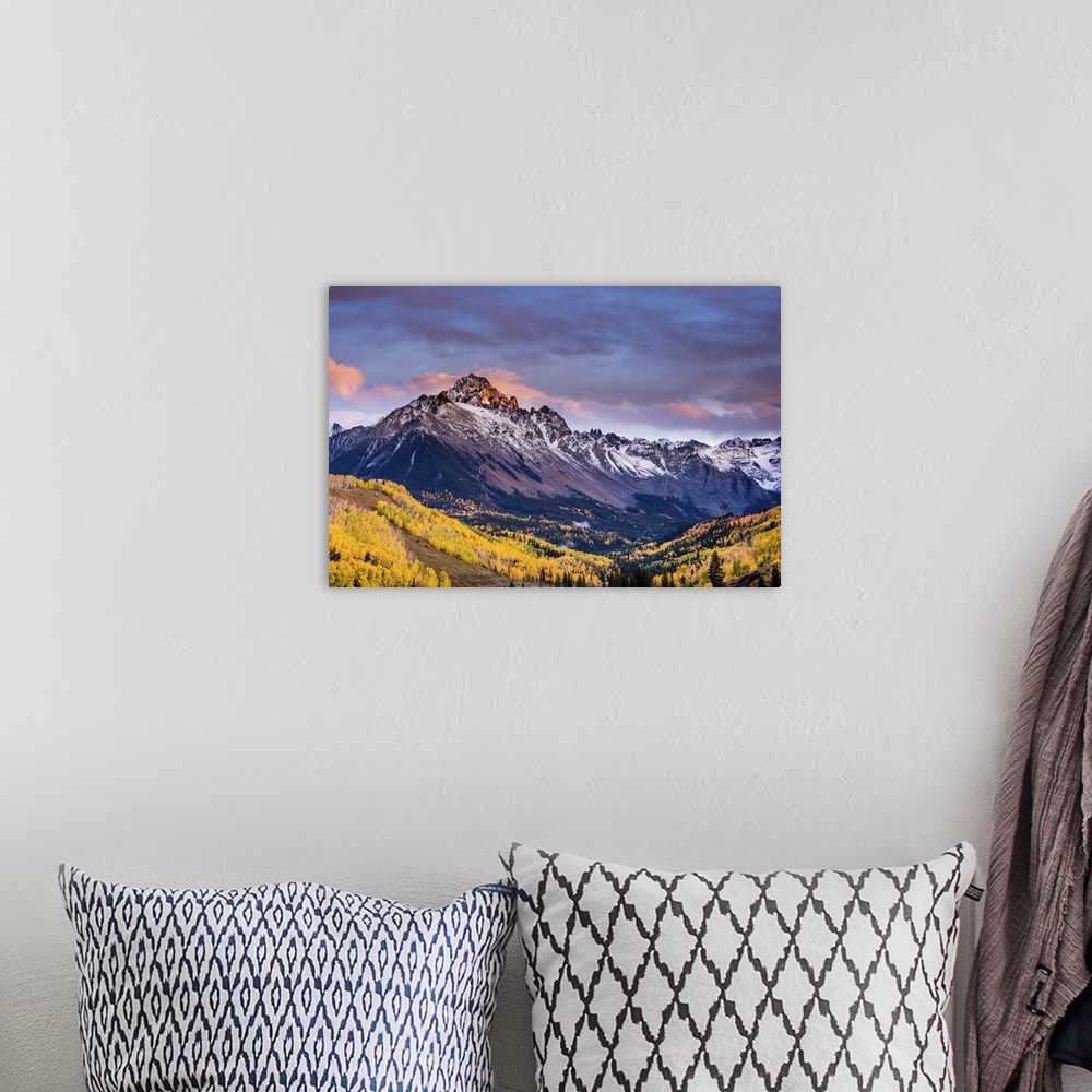 A bohemian room featuring A photograph of mountain under dramatic clouds illuminated by the sunset.