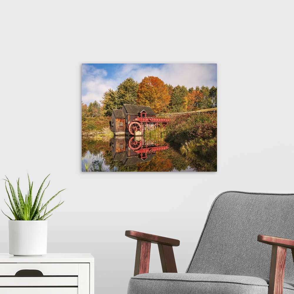 A modern room featuring A photograph of a red water mill in the middle of a forest in autumn foliage.