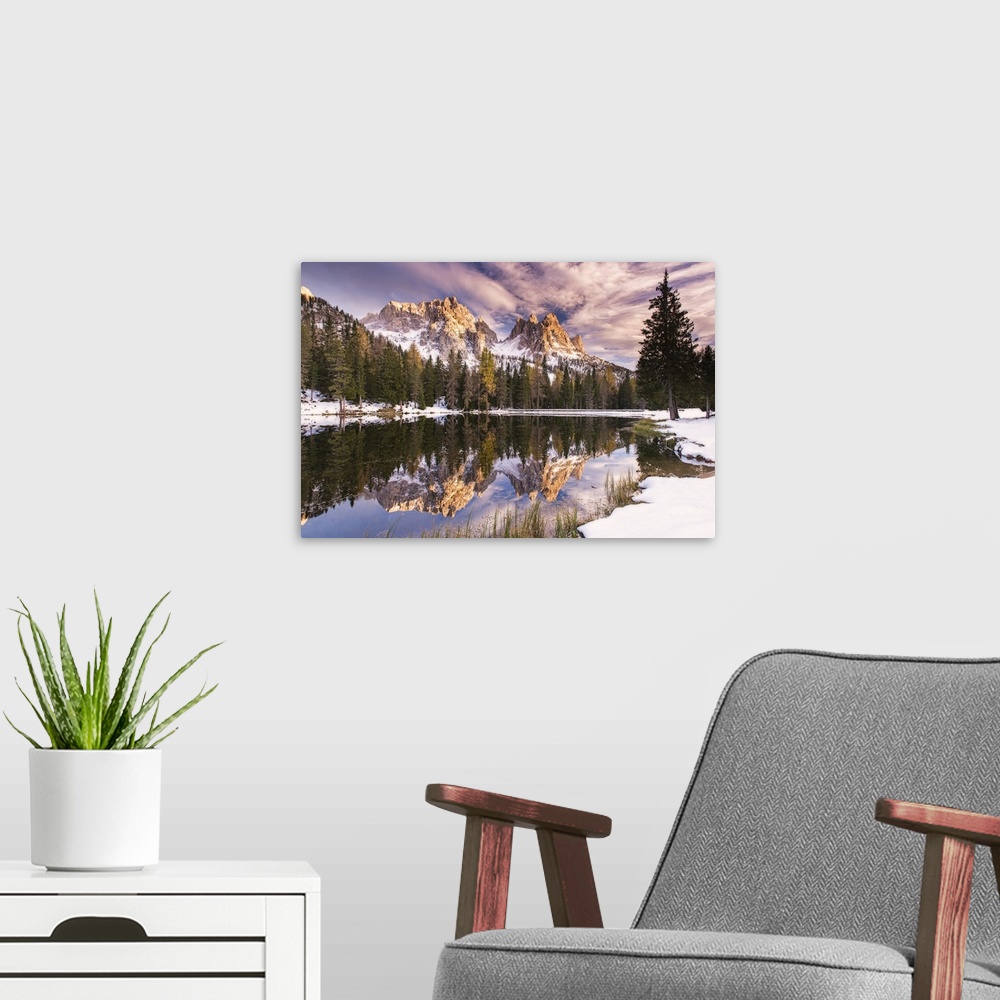 A modern room featuring A photograph of a mountain range and forest reflected in still water, under purple clouds.