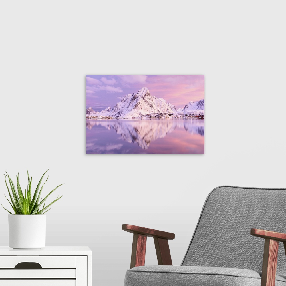 A modern room featuring A photograph of a snow covered mountain range in winter casting a clear reflection in the fjord b...