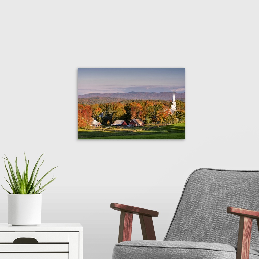 A modern room featuring A photograph of the steeple of a white church sticking high up out of the autumn colored forest.