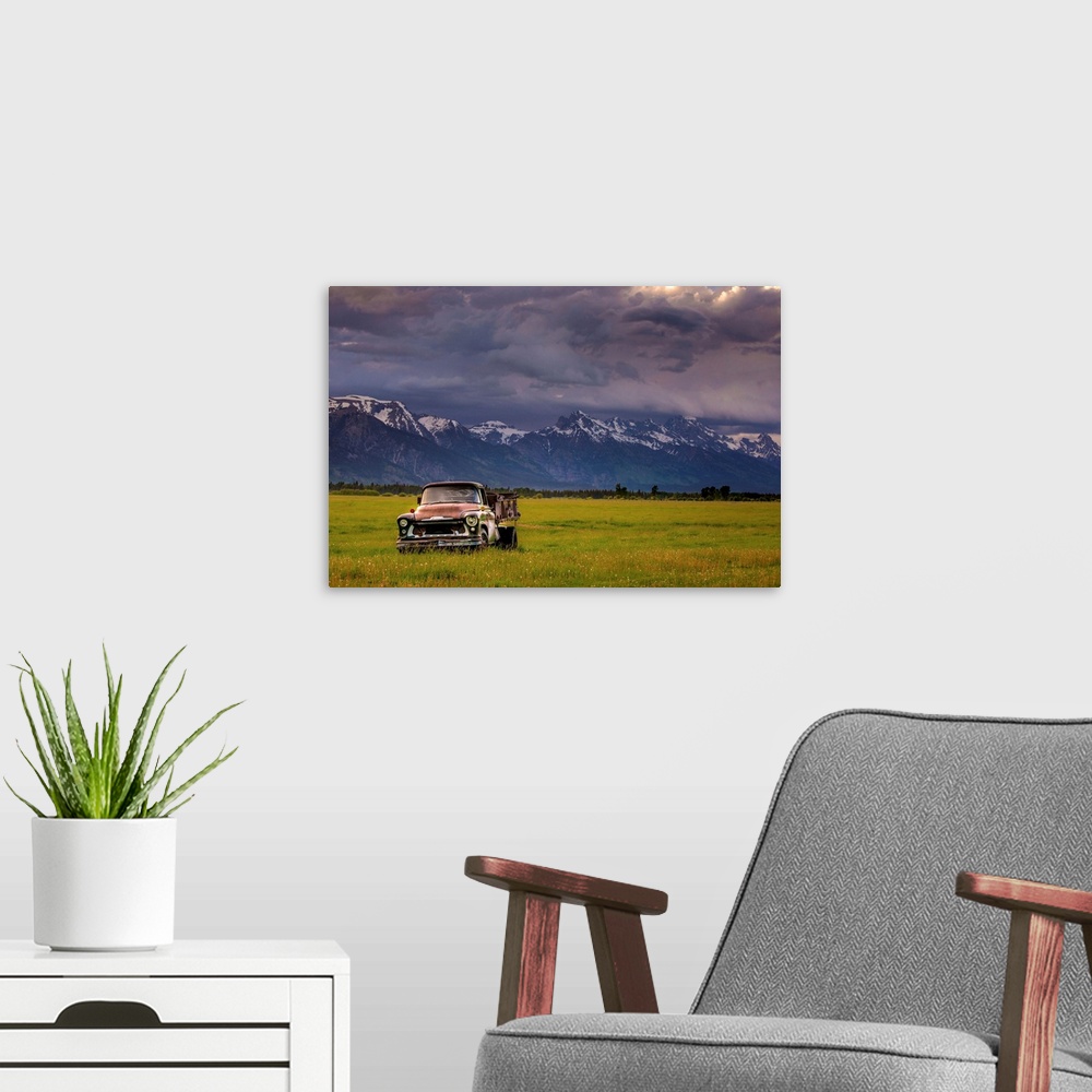 A modern room featuring Landscape photograph of a yellow-green field with an old rusted truck and snow capped mountains i...