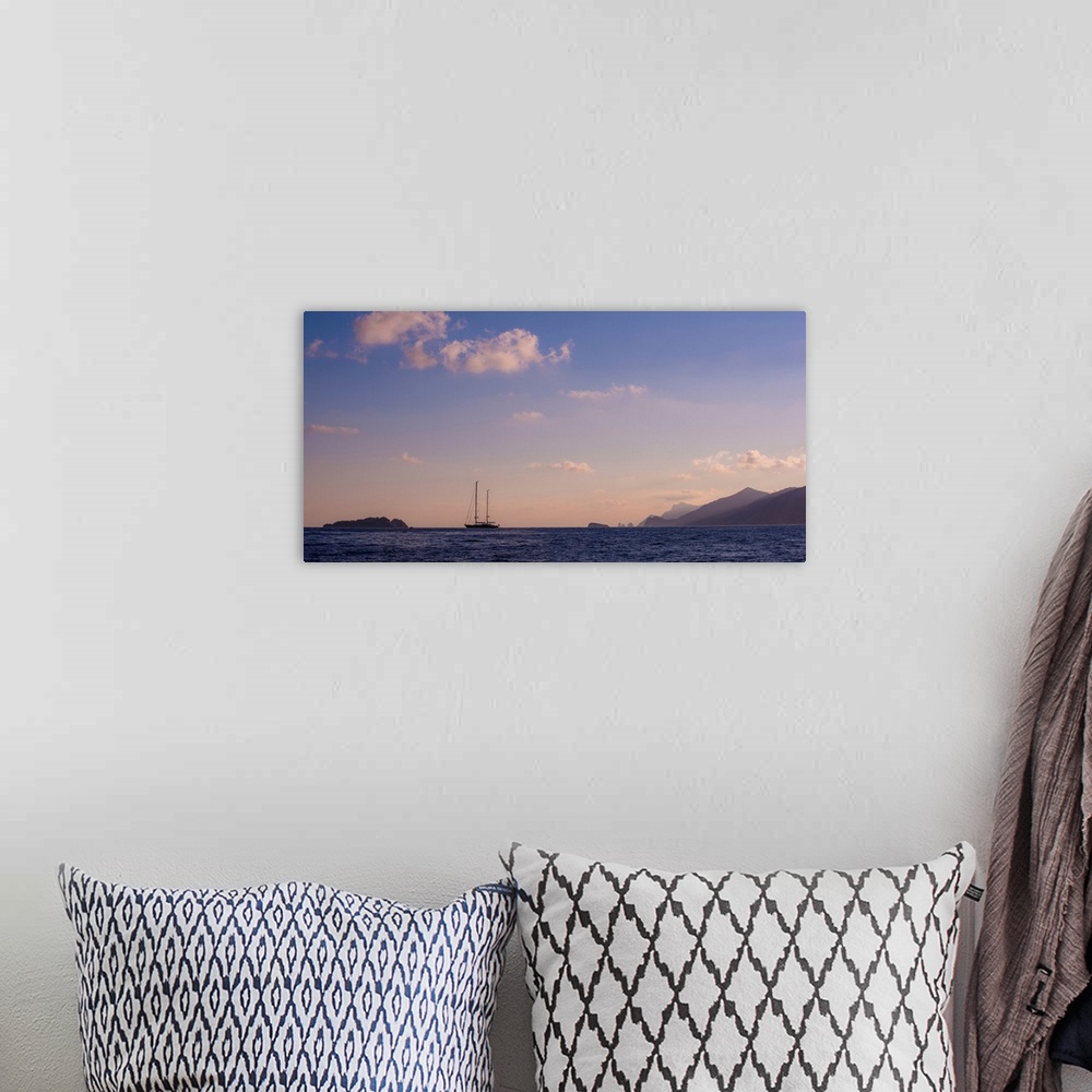 A bohemian room featuring Photograph of a single sailboat in the middle of the ocean with silhouettes of mountains in the d...