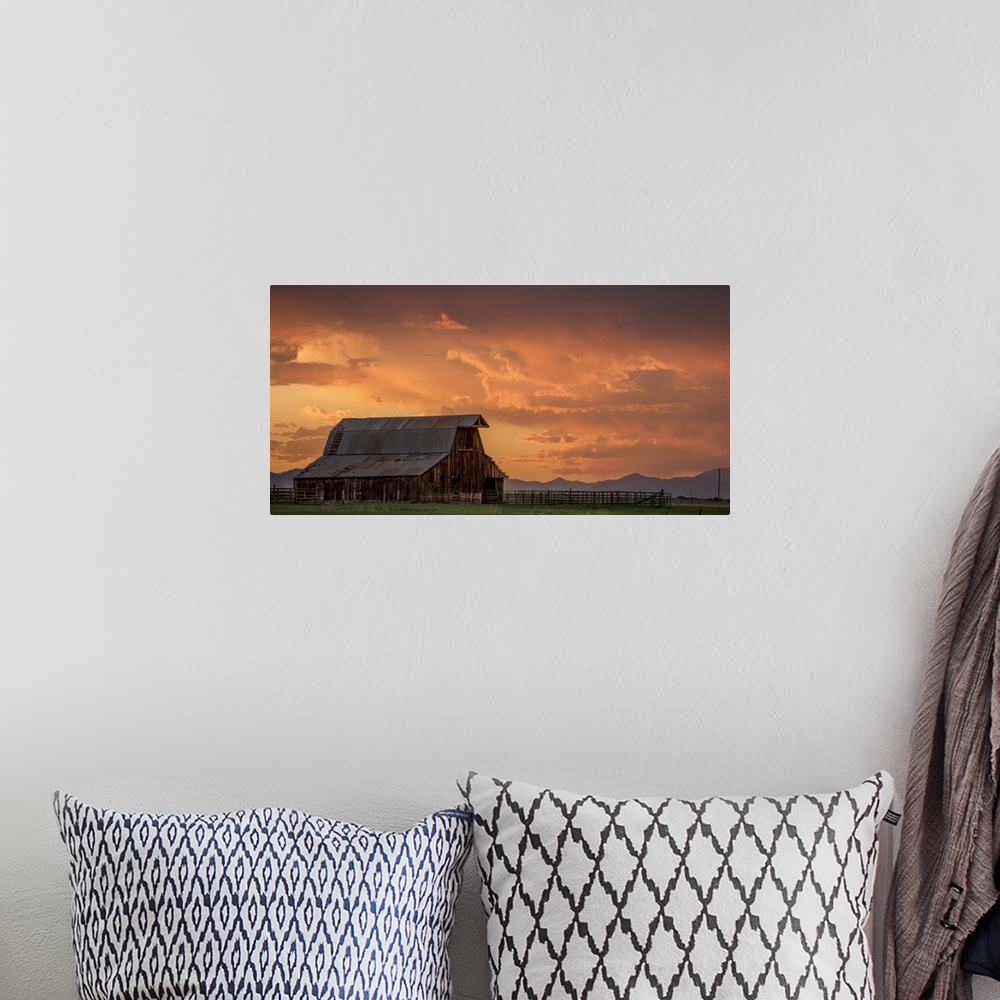 A bohemian room featuring A photograph of an old barn under illuminated clouds of a sunset.