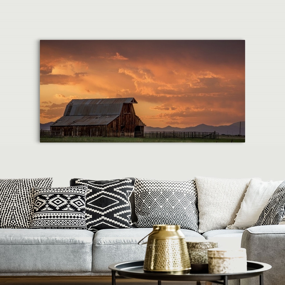 A bohemian room featuring A photograph of an old barn under illuminated clouds of a sunset.