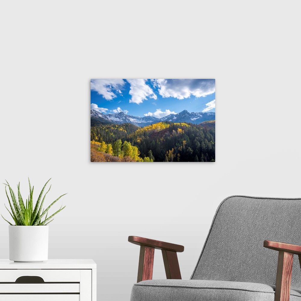 A modern room featuring Landscape photograph of Autumn tree covered hills and snow covered mountains in the distance unde...
