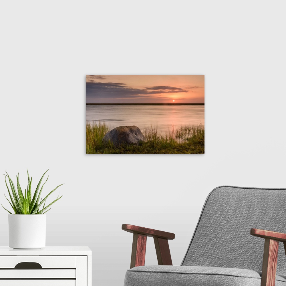 A modern room featuring Landscape photograph of a warm sunset over water with a rock in the foreground.