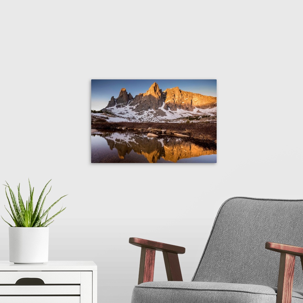 A modern room featuring Landscape photograph of a rocky mountain range covered in snow reflecting onto still water.