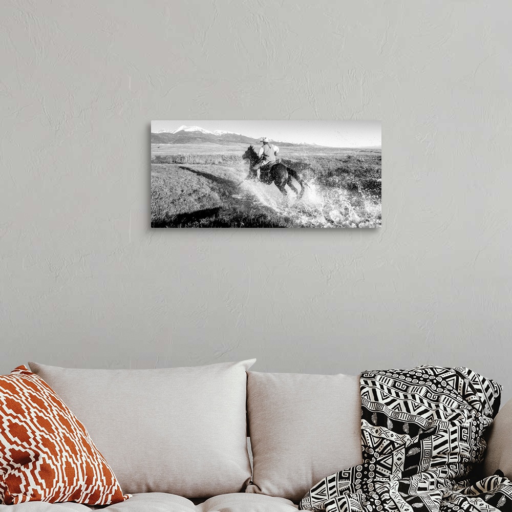 A bohemian room featuring Action photograph of a cowgirl splashing across a river on horseback with snow capped mountains i...