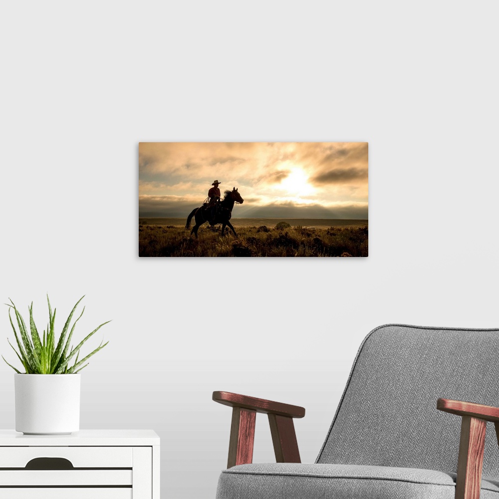 A modern room featuring Photograph of a cowboy riding a horse through a field at sunset.