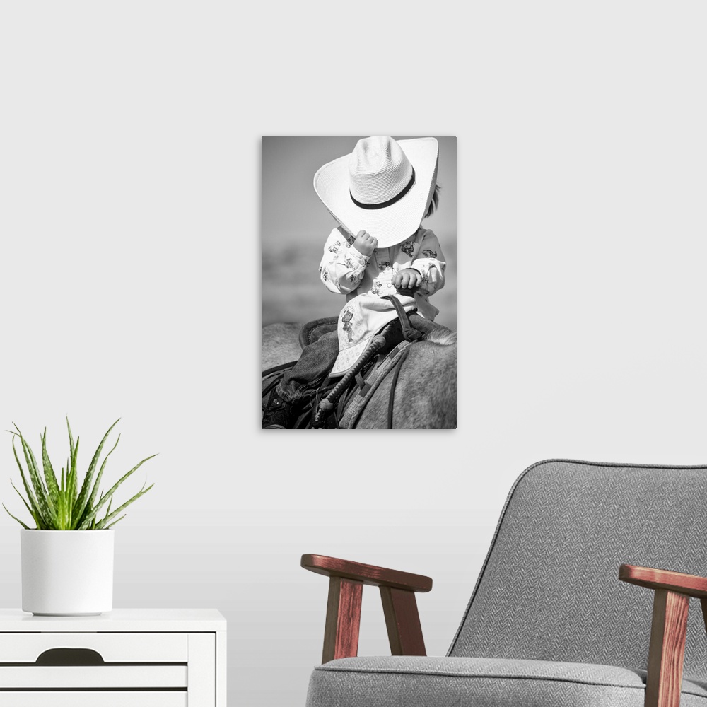 A modern room featuring Very young girl on horseback, tipping big hat that hides her face