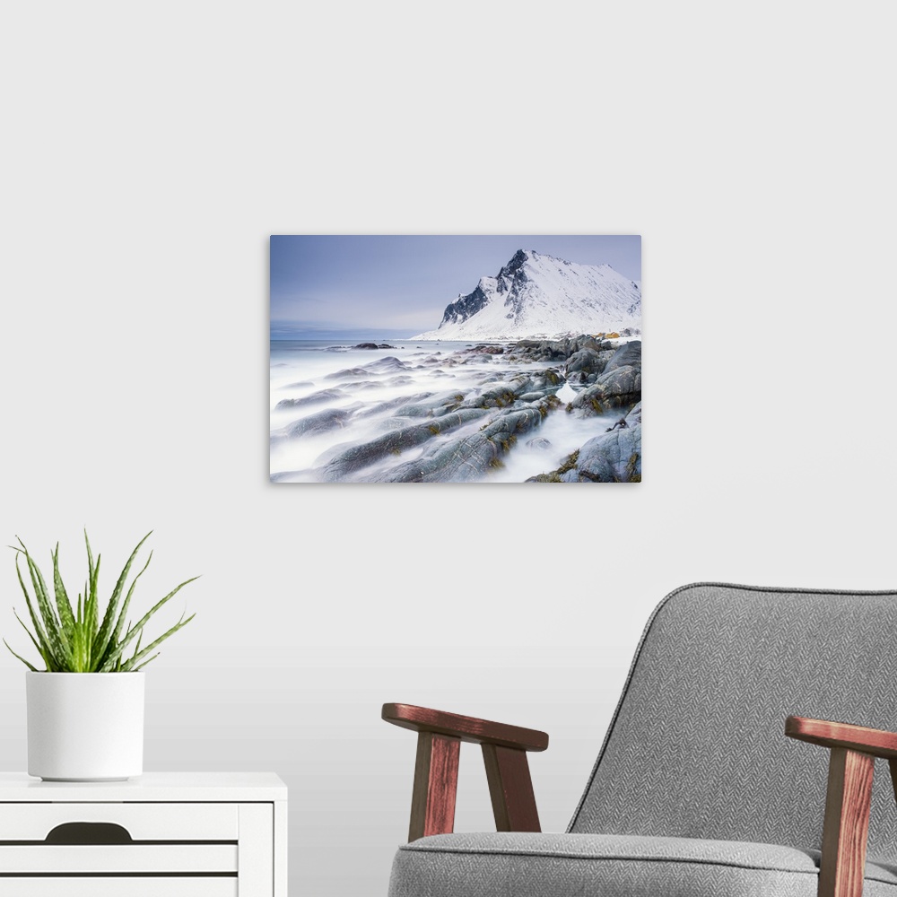 A modern room featuring A photograph of a snow covered mountain seen from a rocky shoreline with motion blurred water cau...