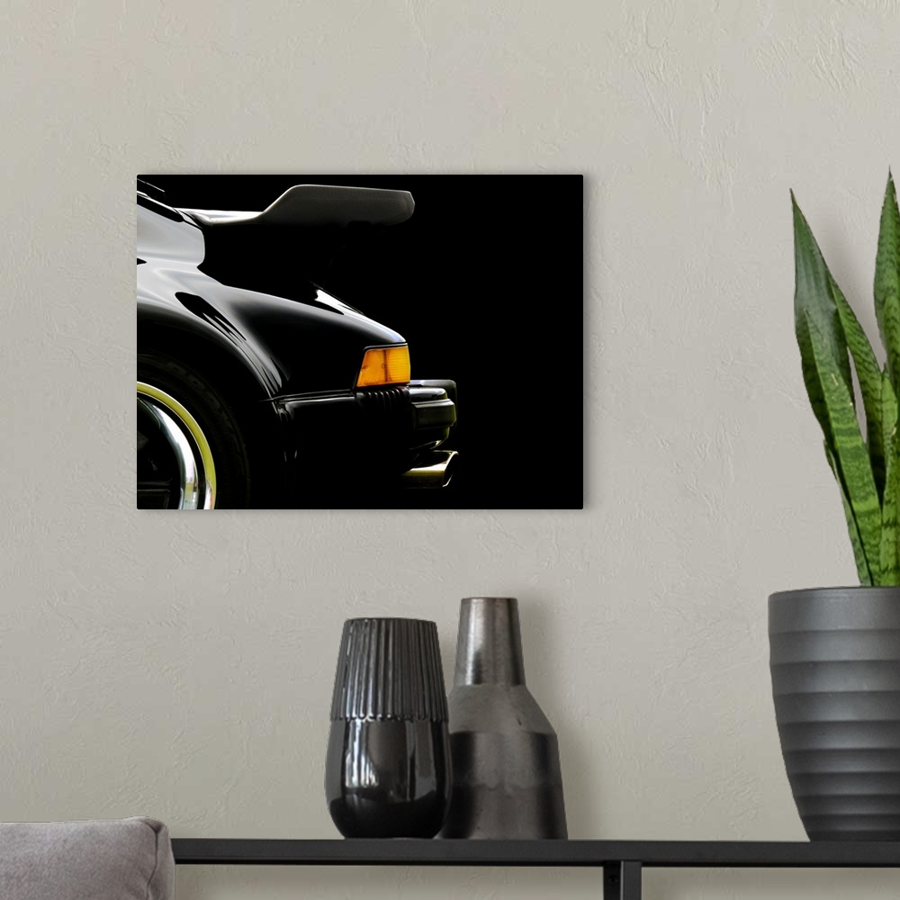 A modern room featuring Photograph of the rear and back wing of a black 78 Porsche 930 with a solid black background.