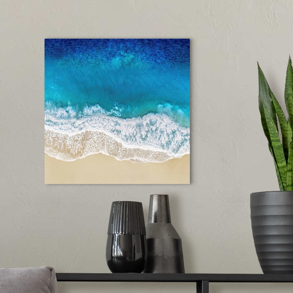 A modern room featuring One artwork in a series of aerial shots of a beach as blue waves break upon the shore.