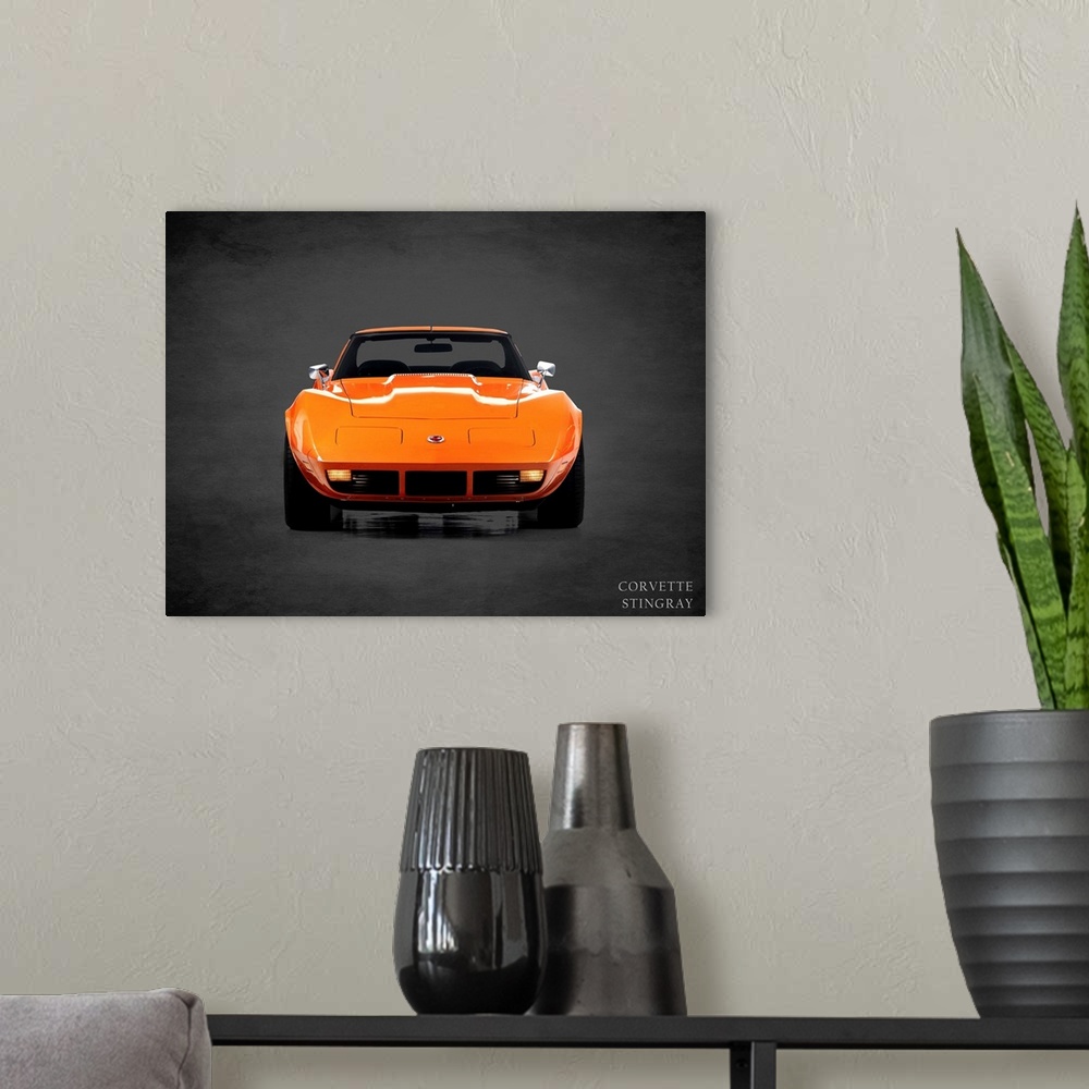 A modern room featuring Photograph of an orange 1974 Chevrolet Corvette Stingray printed on a black background with a dar...